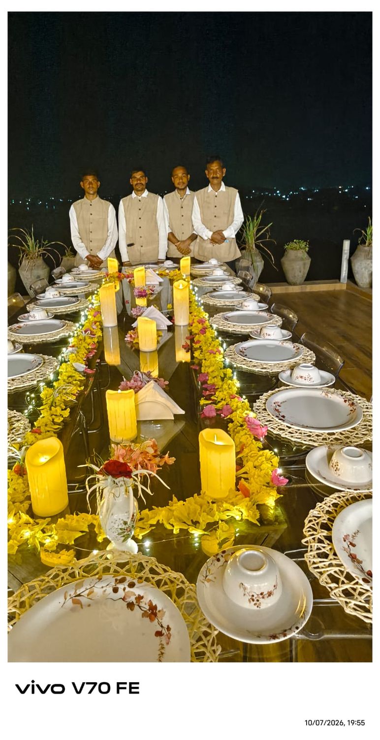 A candlelit dinner table with staff ready, the lake behind