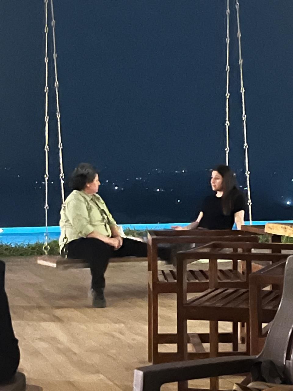 Two women on a swing by the pool at night